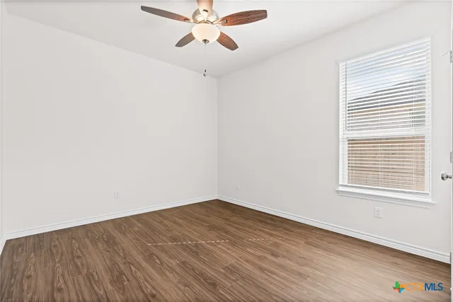 an empty room with wooden floor fan and windows