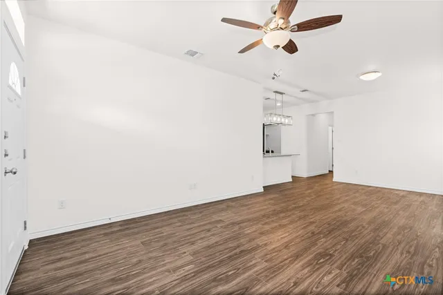 an empty room with wooden floor ceiling fan and windows