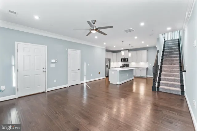 a view of an empty room with wooden floor and a kitchen