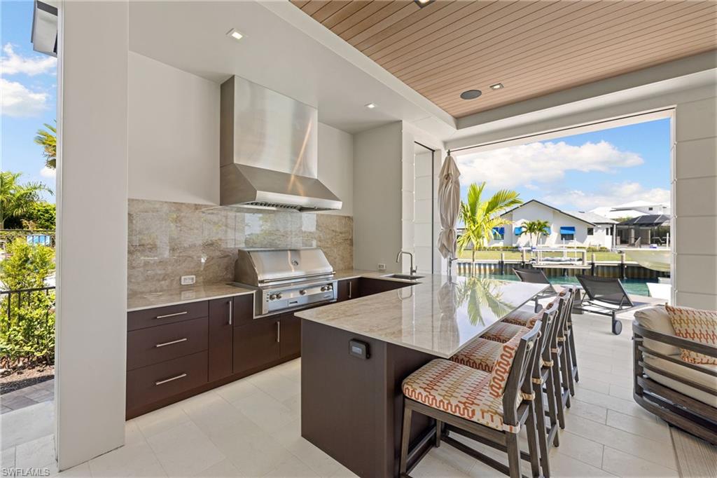 2345 Tarpon Road Naples, FL 34102 - Photo 17 of 43 Kitchen featuring dark wood finish cabinets, light stone countertops, a kitchen bar, a peninsula, and wooden ceiling
