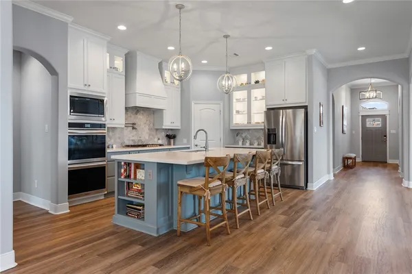 a large kitchen with stainless steel appliances a large center island wooden floor and a view of living room