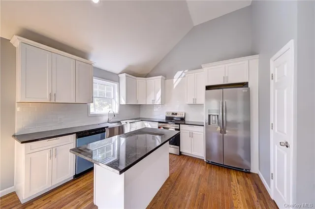 a open kitchen with granite countertop a stove top oven a sink dishwasher a refrigerator and white cabinets with wooden floor