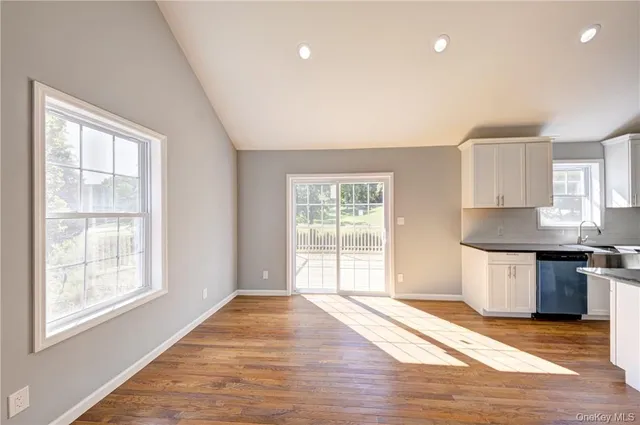 a view of empty room with wooden floor and kitchen view