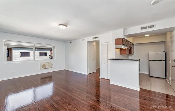 a view of empty room with wooden floor and kitchen