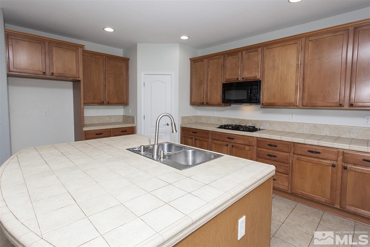 581 Alydar Court Reno, NV 89521 - Photo 5 of 22 a kitchen with granite countertop a sink and a stove top oven with wooden cabinets