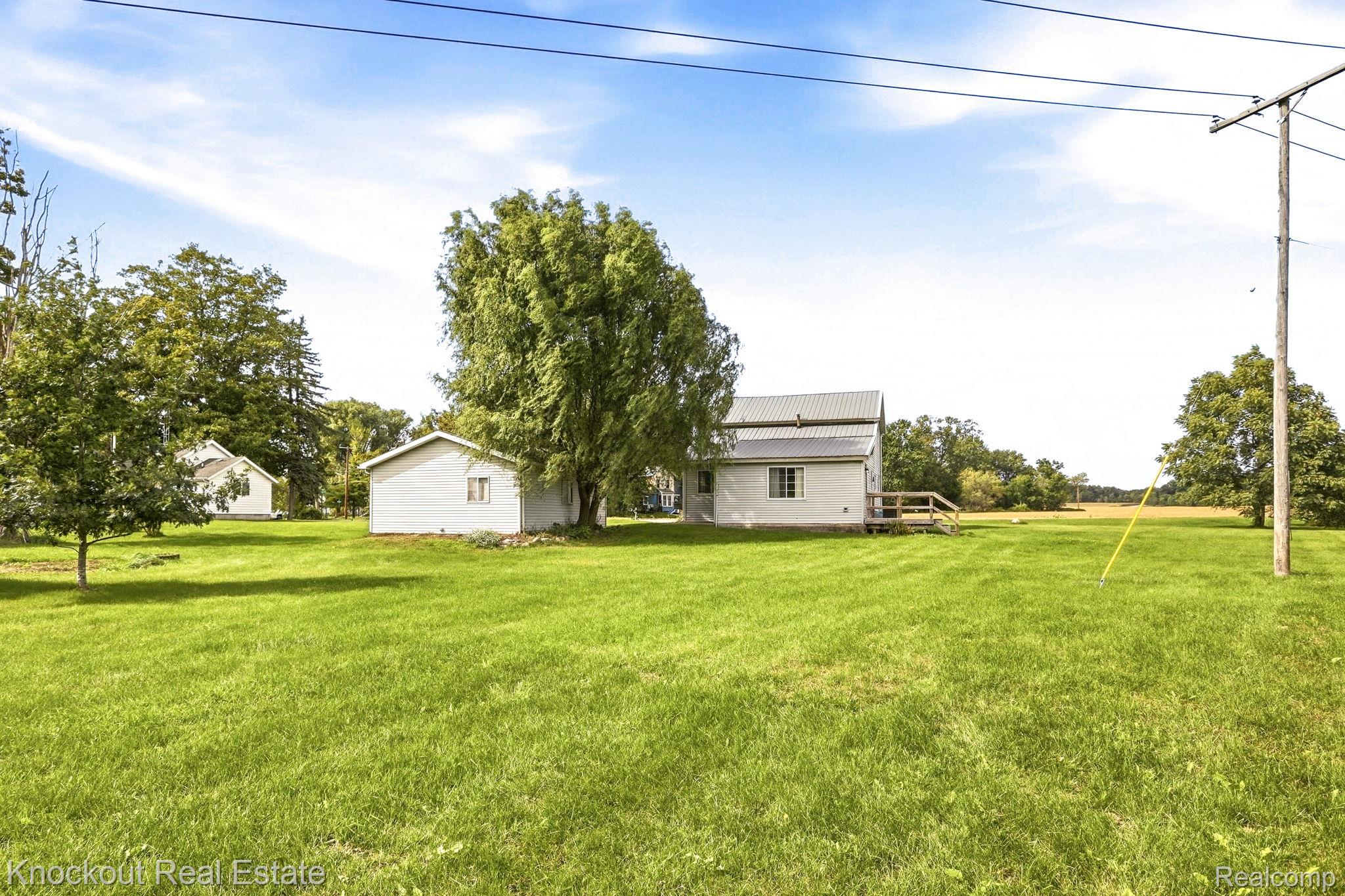 8771 Van Cleve Road Vassar, MI 48768 - Photo 39 of 44 Expansive green lawn with mature trees, featuring a white siding structure with a metal roof, an additional white siding outbuilding, and a wood deck