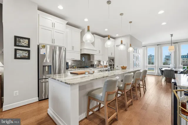 a kitchen with stainless steel appliances kitchen island granite countertop a refrigerator a stove a sink a dining table and chairs with wooden floor