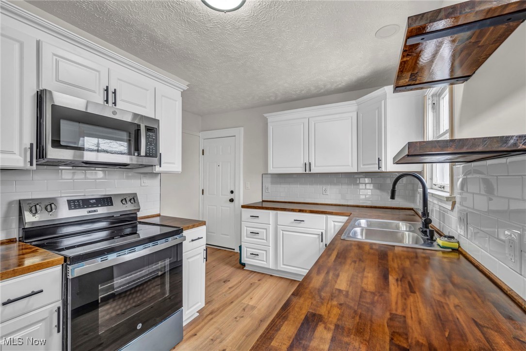 3577 Warren Road Cleveland, OH 44111 - Photo 2 of 17 Kitchen featuring butcher block counters, appliances with stainless steel finishes, white cabinetry, a sink, and light wood-type flooring