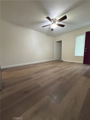 a view of an empty room with wooden floor and a ceiling fan