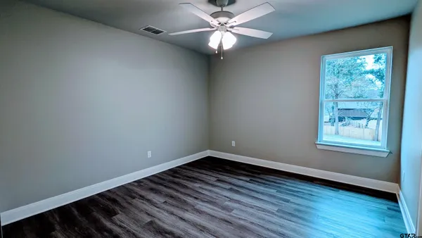 an empty room with wooden floor fan and windows