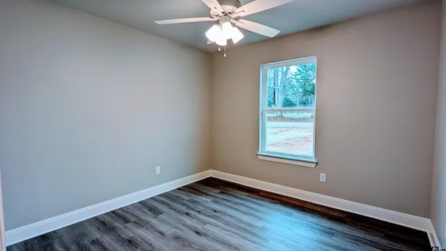 an empty room with wooden floor chandelier fan and windows