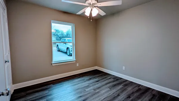 an empty room with wooden floor chandelier fan and windows