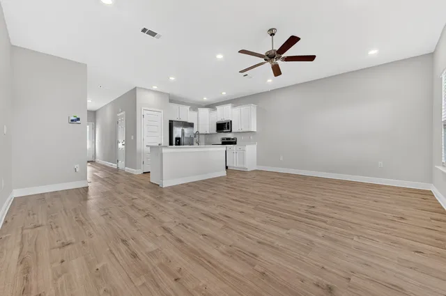 a view of a livingroom with kitchen appliances and a ceiling fan