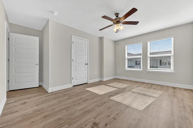an empty room with wooden floor ceiling fan and windows