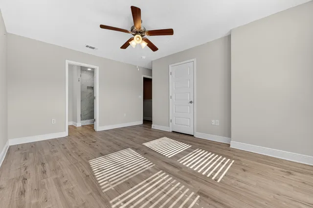 a view of an empty room with wooden floor ceiling fan