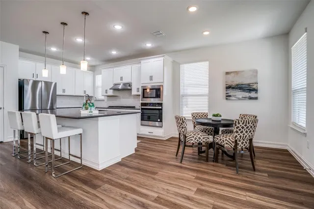 a kitchen with stainless steel appliances kitchen island granite countertop a refrigerator a stove a dining table and chairs with wooden floor