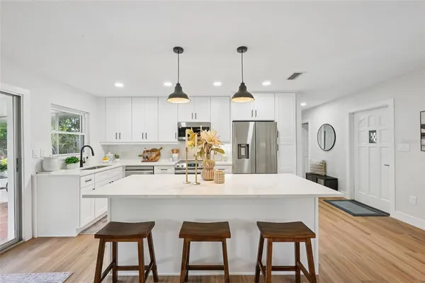 a kitchen with stainless steel appliances granite countertop a refrigerator a stove top oven a sink dishwasher and white cabinets with wooden floor