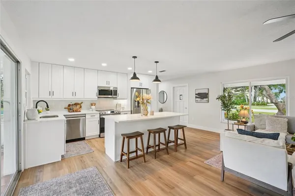 a kitchen with stainless steel appliances a sink a stove a refrigerator cabinets a dining table and chairs