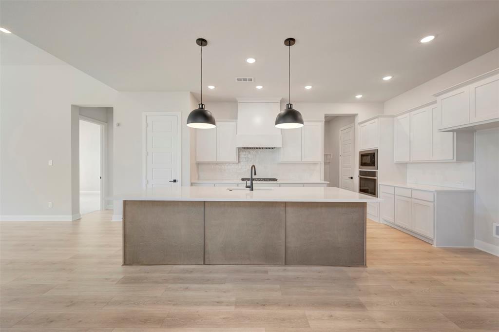 3575 Redbud Flower Trail Venus, TX 76084 - Photo 13 of 36 Two tone kitchen featuring a kitchen island with sink, light wood-type flooring, stainless steel appliances, backsplash, and dual tone cabinets