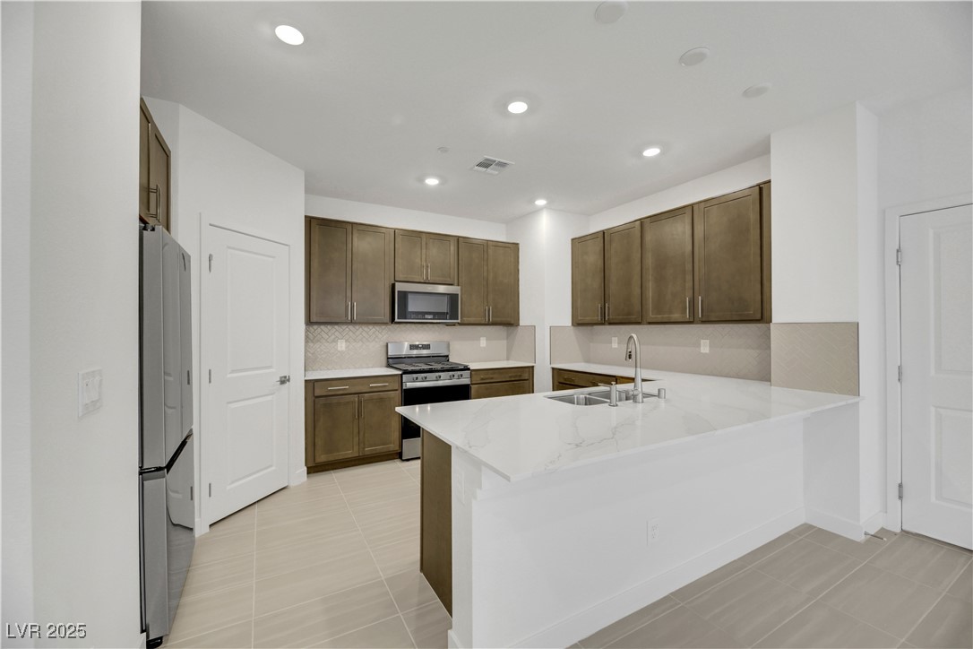 2770 Alfena Place Henderson, NV 89044 - Photo 12 of 26 Kitchen with stainless steel appliances, backsplash, light stone countertops, light tile patterned flooring, and a peninsula