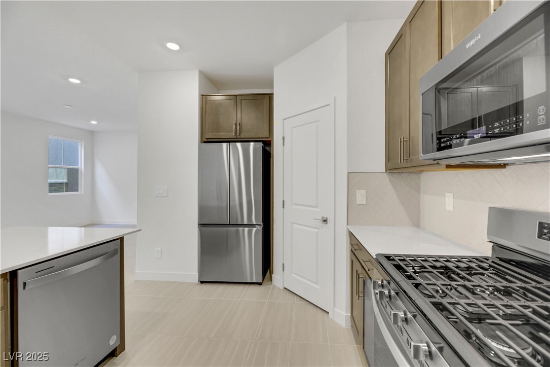 2770 Alfena Place Henderson, NV 89044 - Photo 13 of 26 Kitchen with appliances with stainless steel finishes, recessed lighting, tasteful backsplash, light stone countertops, and light tile patterned flooring