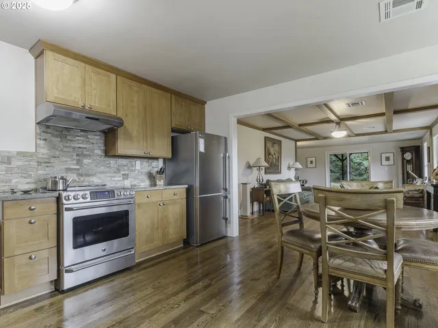 a kitchen with stainless steel appliances granite countertop a stove top oven a sink a dining table and chairs with wooden floor