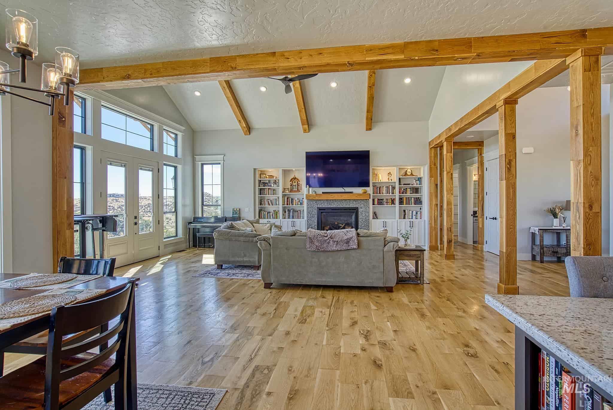 876 Coyote Gulch Road Adrian, OR 97901 - Photo 30 of 50 Vaulted ceiling with exposed wood beams, wood-finish flooring, built-in shelving, stone-surround fireplace, and double French doors