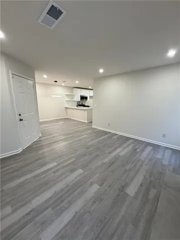 an empty room with wooden floor kitchen view and windows