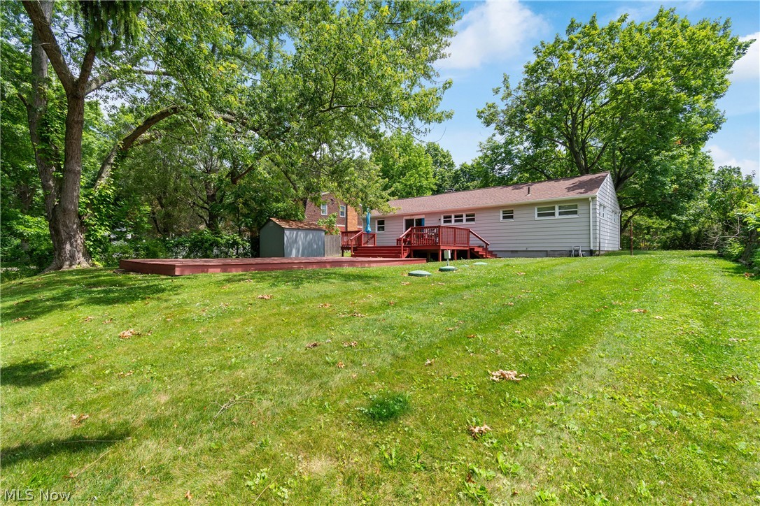 5768 Nolley Road Akron, OH 44319 - Photo 31 of 38 Expansive backyard featuring a large green lawn, mature trees, a multi-level red-toned wooden deck, and a detached storage shed