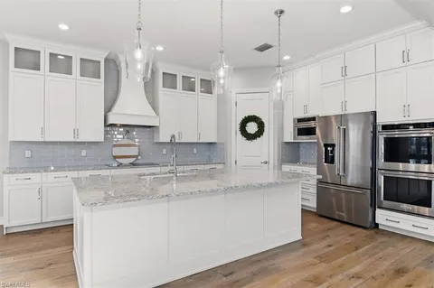 a kitchen with stainless steel appliances granite countertop a refrigerator a sink dishwasher a stove and white cabinets with wooden floor