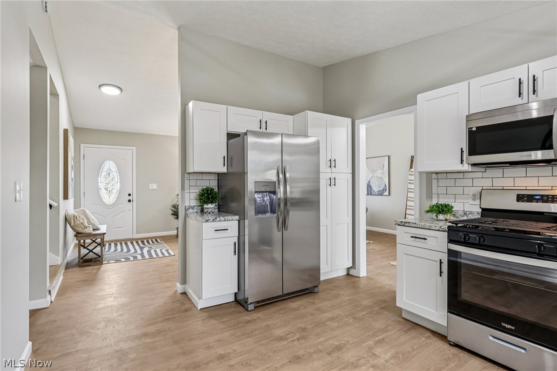 Kitchen with stainless steel appliances, white cabinets, decorative backsplash, light wood finished floors, and light stone counters