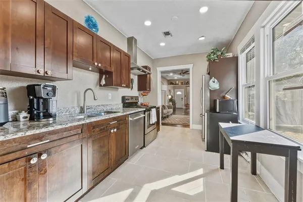 a kitchen with stainless steel appliances granite countertop a stove top oven a sink a refrigerator and white cabinets with wooden floor