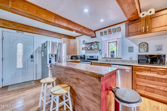 a kitchen with stainless steel appliances granite countertop a refrigerator a sink dishwasher a dining table and chairs with wooden floor