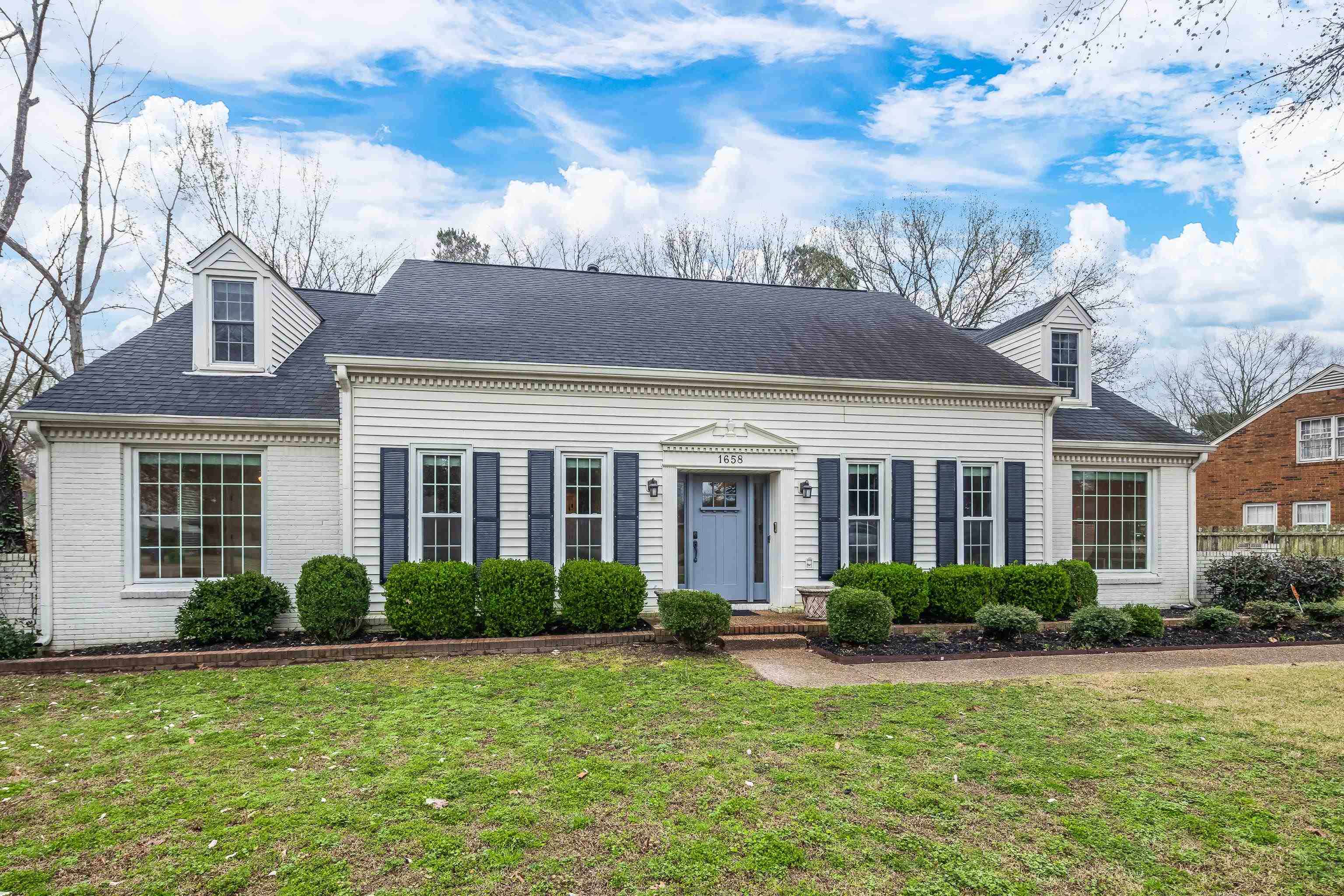 New england style home featuring roof with shingles, a front yard, and brick siding