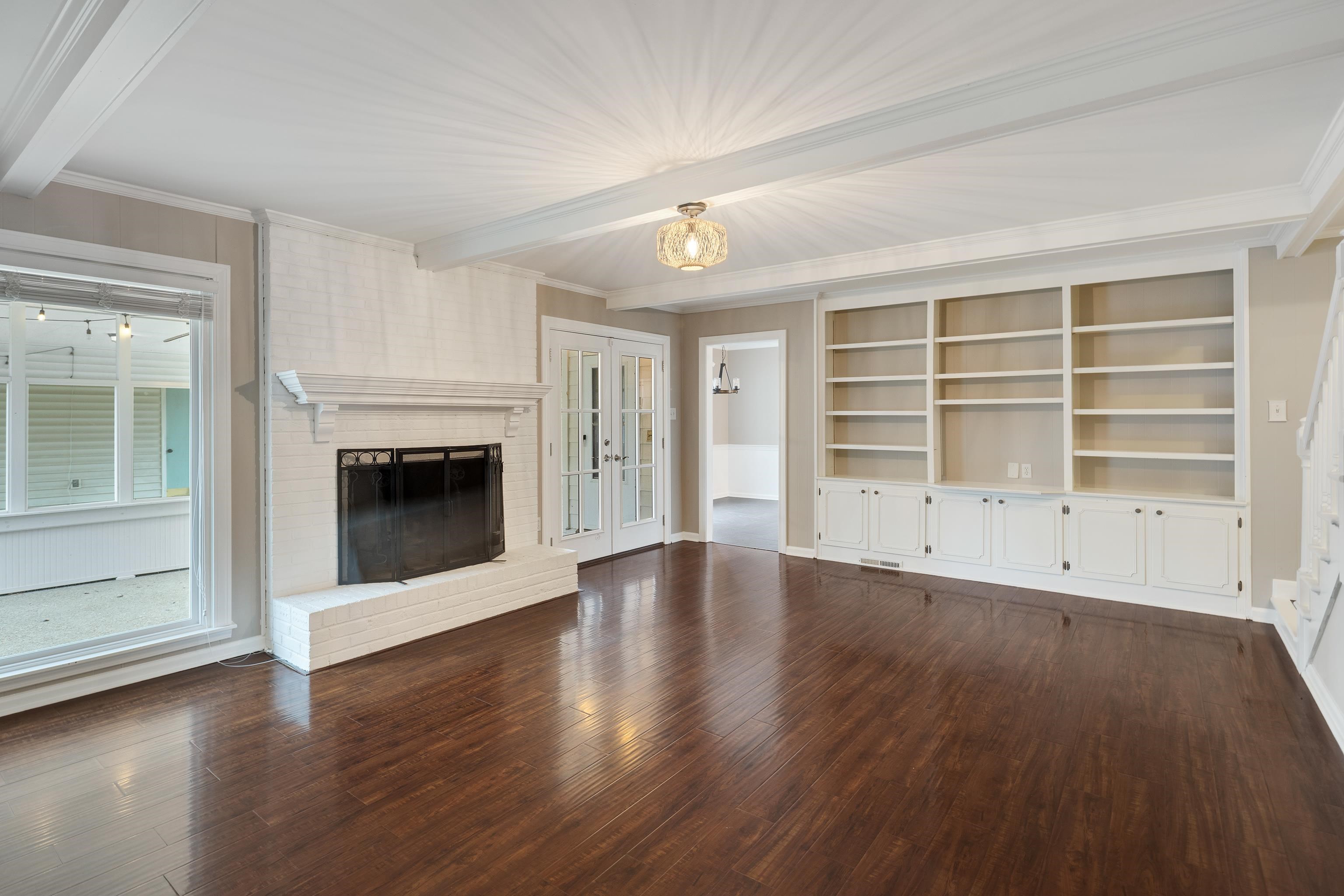 1658 Miller Farms Road Germantown, TN 38138 - Photo 14 of 39 Unfurnished living room featuring a brick fireplace, french doors, dark wood-style flooring, beamed ceiling, and ornamental molding