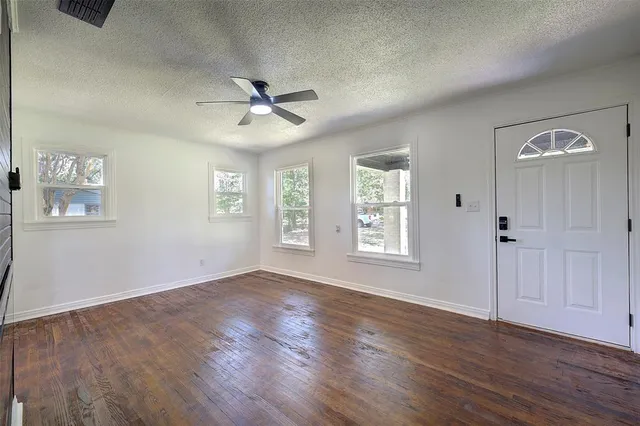 an empty room with wooden floor chandelier fan and windows