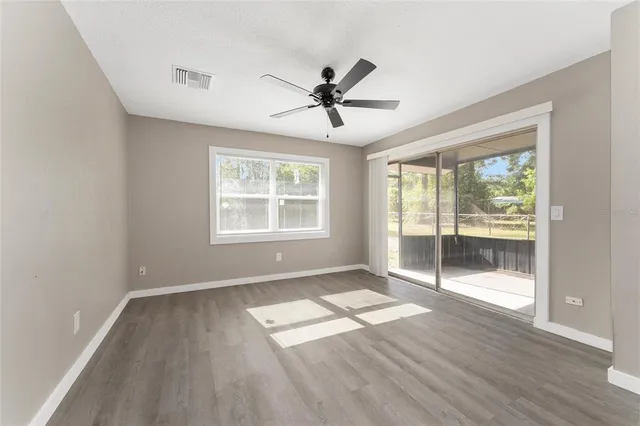 an empty room with wooden floor fan and windows