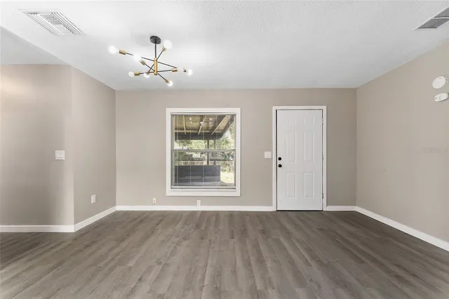 an empty room with wooden floor chandelier fan and windows