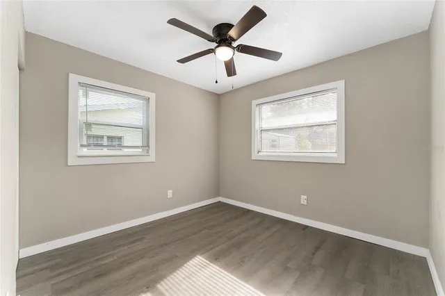 a view of an empty room with wooden floor and a ceiling fan