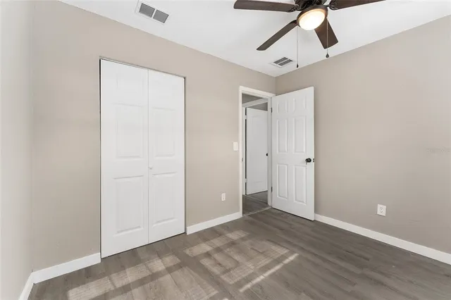 an empty room with wooden floor ceiling fan and windows