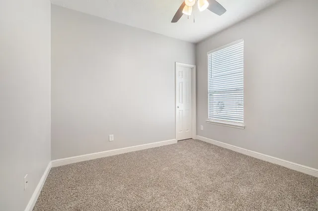 an empty room with a chandelier fan and windows