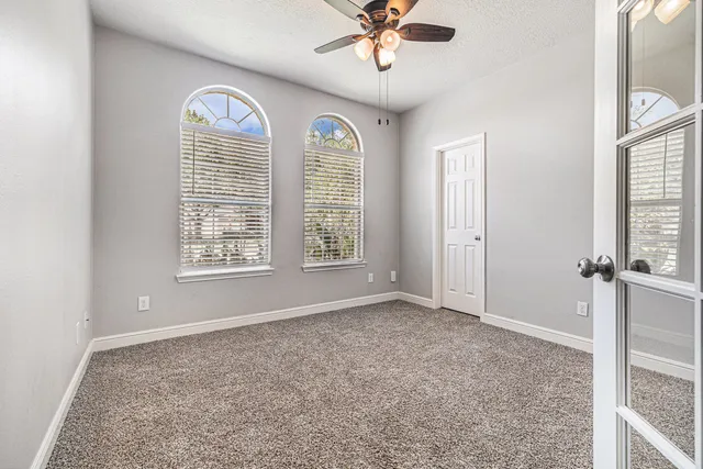 an empty room with chandelier fan and windows
