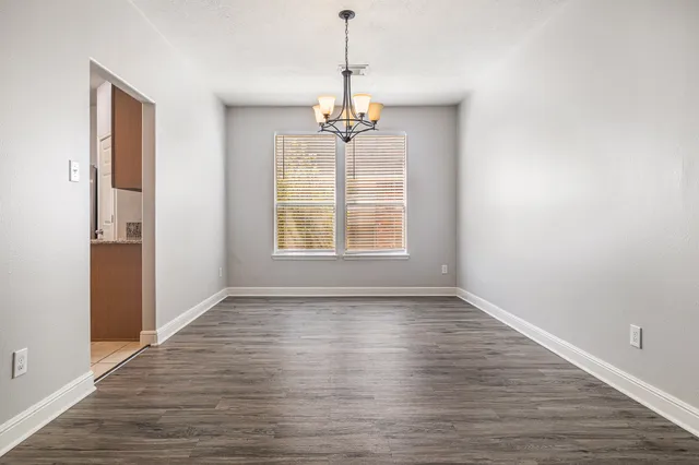 an empty room with wooden floor chandelier and windows