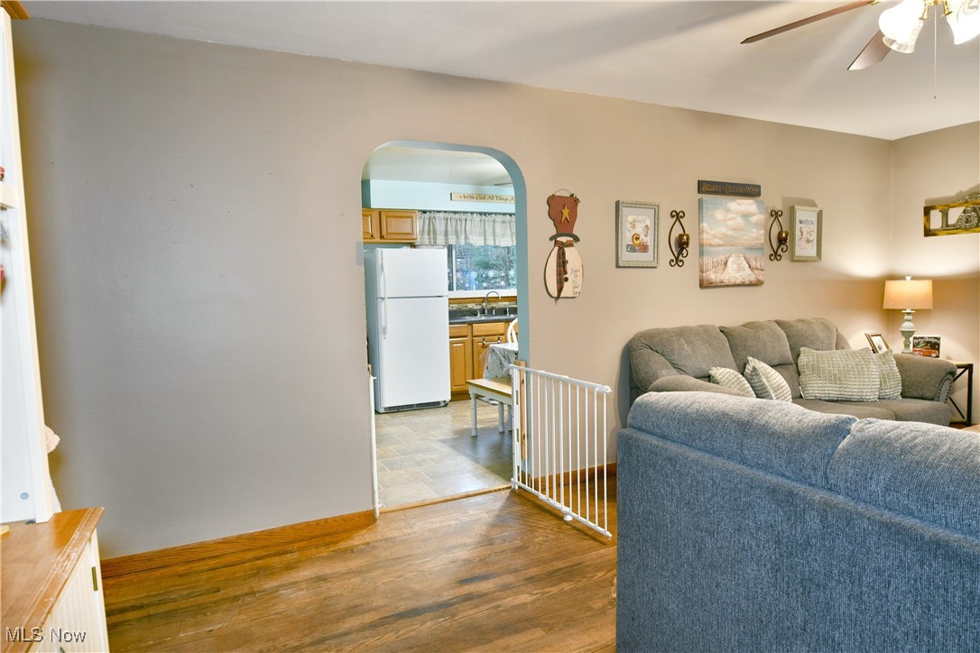 Living room with arched walkways, ceiling fan, and wood finished floors