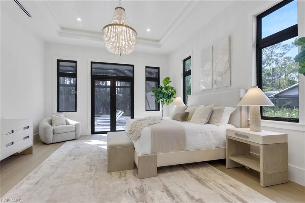5174 Sycamore Drive Naples, FL 34119 - Photo 23 of 50 a spacious bedroom with a bed a chandelier and large window