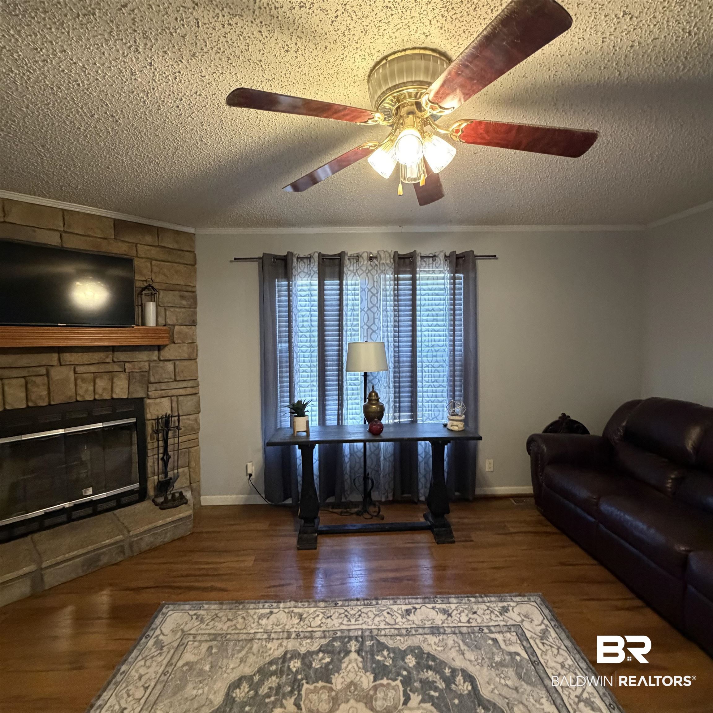 447 Sugar Hill Road Monroeville, AL 36460 - Photo 12 of 27 Living room with ornamental molding, dark wood-style floors, a ceiling fan, a textured ceiling, and a stone fireplace