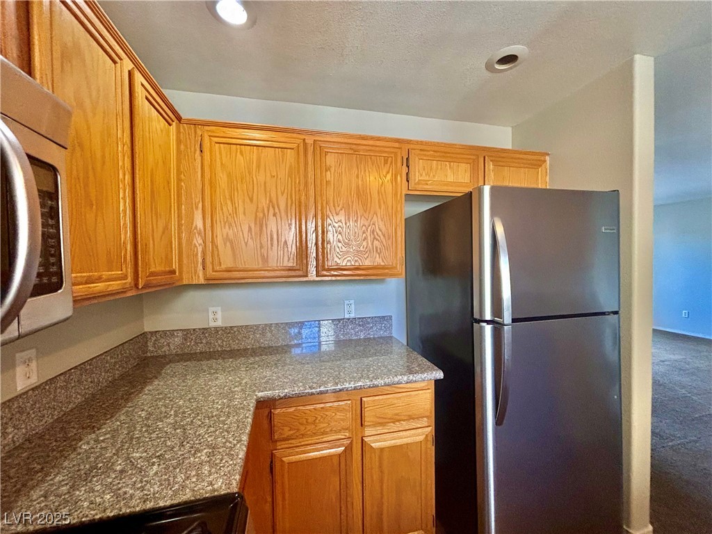 2011 Cutlass Drive Henderson, NV 89014 - Photo 17 of 41 Kitchen with stainless steel appliances, brown cabinetry, carpet floors, dark stone countertops, and recessed lighting
