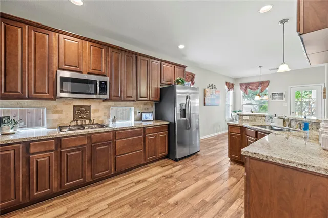 a kitchen with granite countertop wooden cabinets a stove a oven a refrigerator and a oven with wooden floor