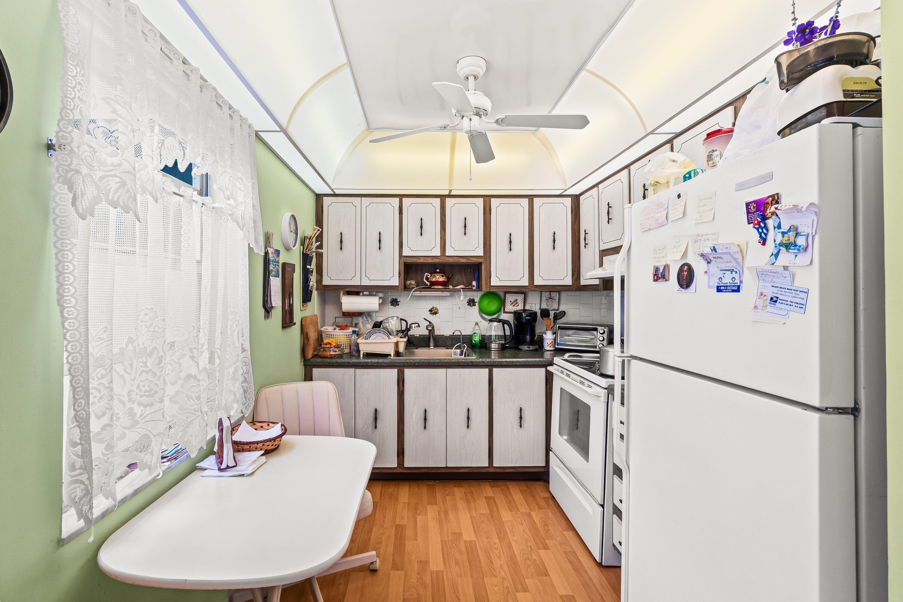 508 Normandy Lane, Unit 508 Delray Beach, FL 33484 - Photo 7 of 25 a kitchen with granite countertop a white refrigerator a sink dishwasher a dining table and chairs with wooden floor