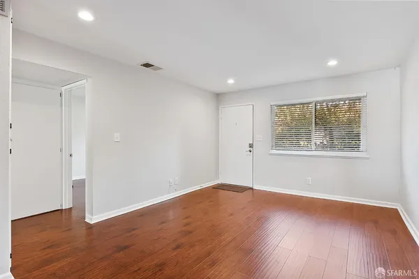 a view of an empty room with wooden floor and a window